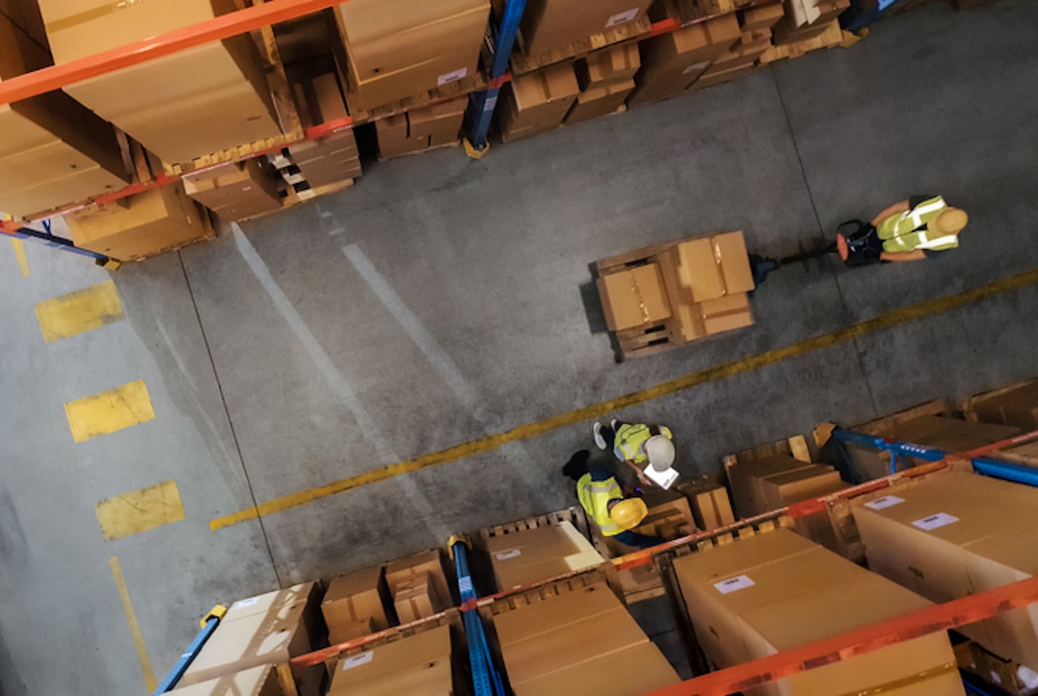 Top-Down View: Worker Moves Cardboard Boxes using Hand Pallet Truck, Walking between Rows of Shelves with Goods in Retail Warehouse. People Work in Product Distribution Logistics Center